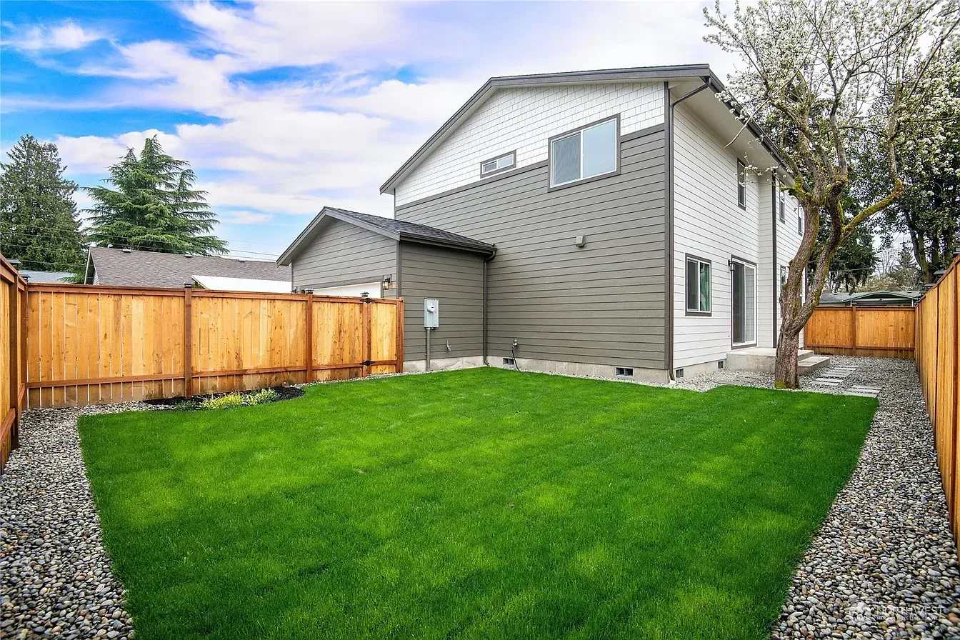 Backyard of a house with a green lawn, wooden fence, and gray siding on a sunny day.