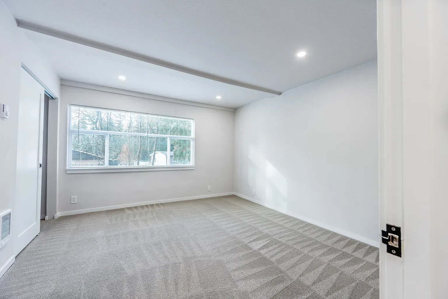 Empty white bedroom with carpet and large window overlooking trees