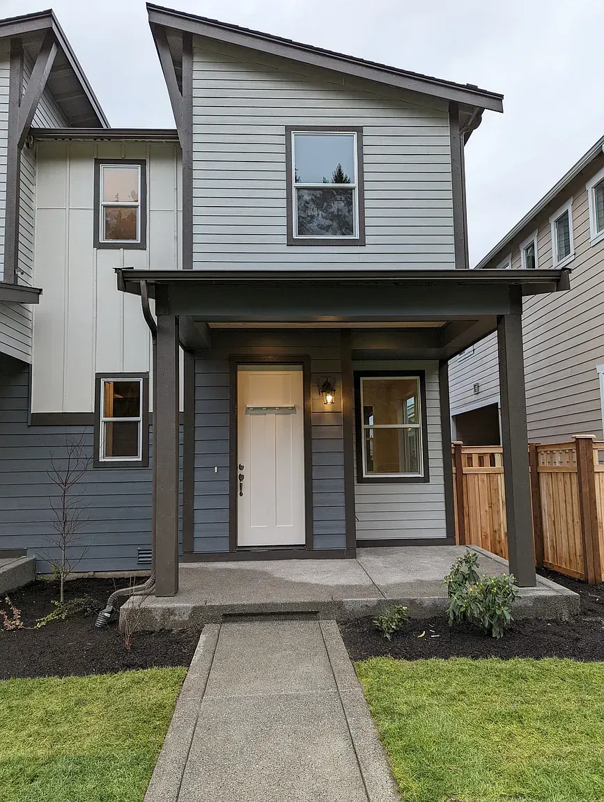 Two-story townhome with grey and white siding, front porch, and a walkway leading to the front door.