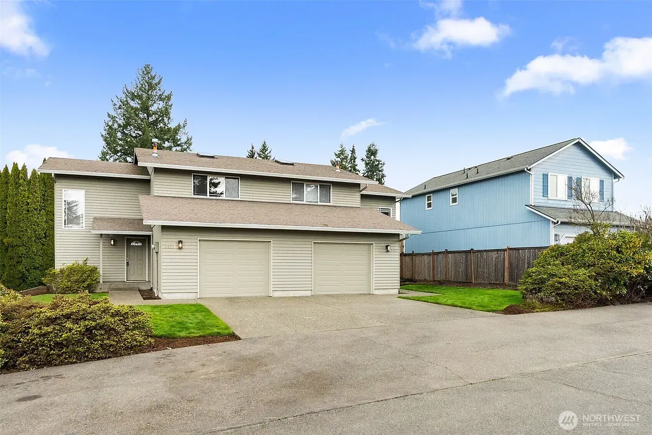 Two-story suburban house with beige siding, attached garage, and driveway under a blue sky