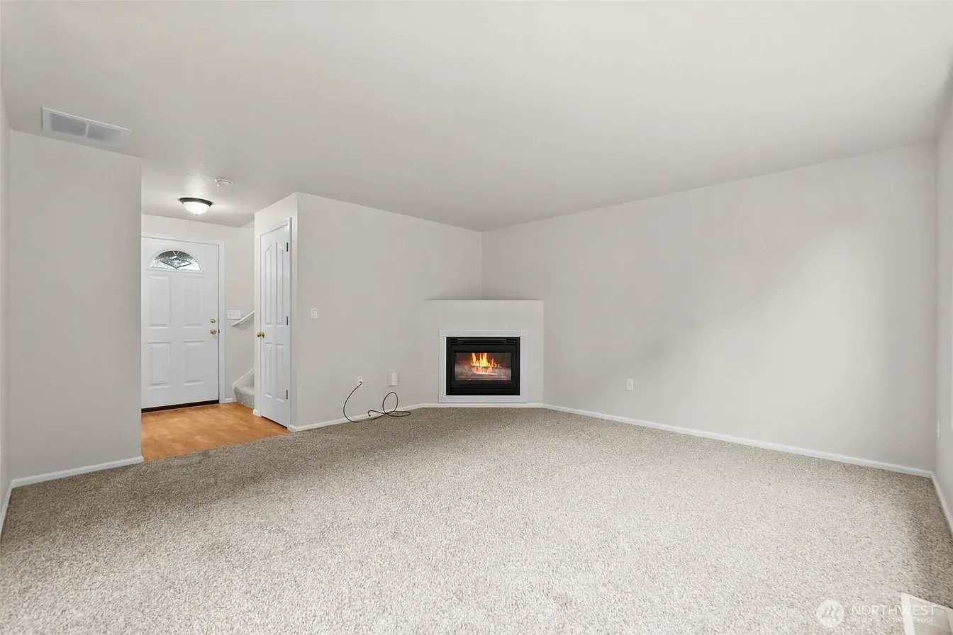 Empty beige living room with carpet, fireplace, and doorway to a hall with wood floors