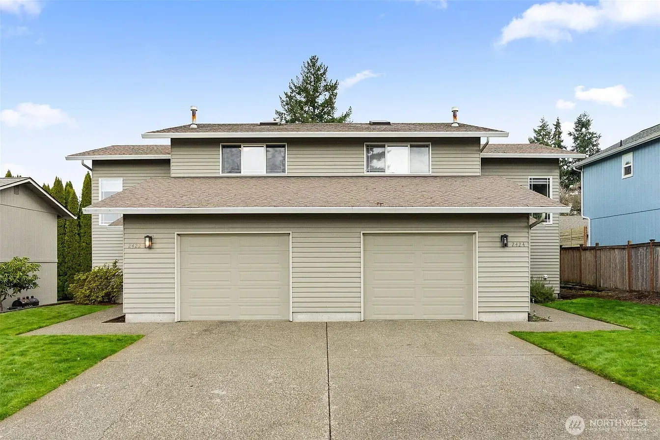 Two-story beige townhouse with three garage doors and a gravel driveway