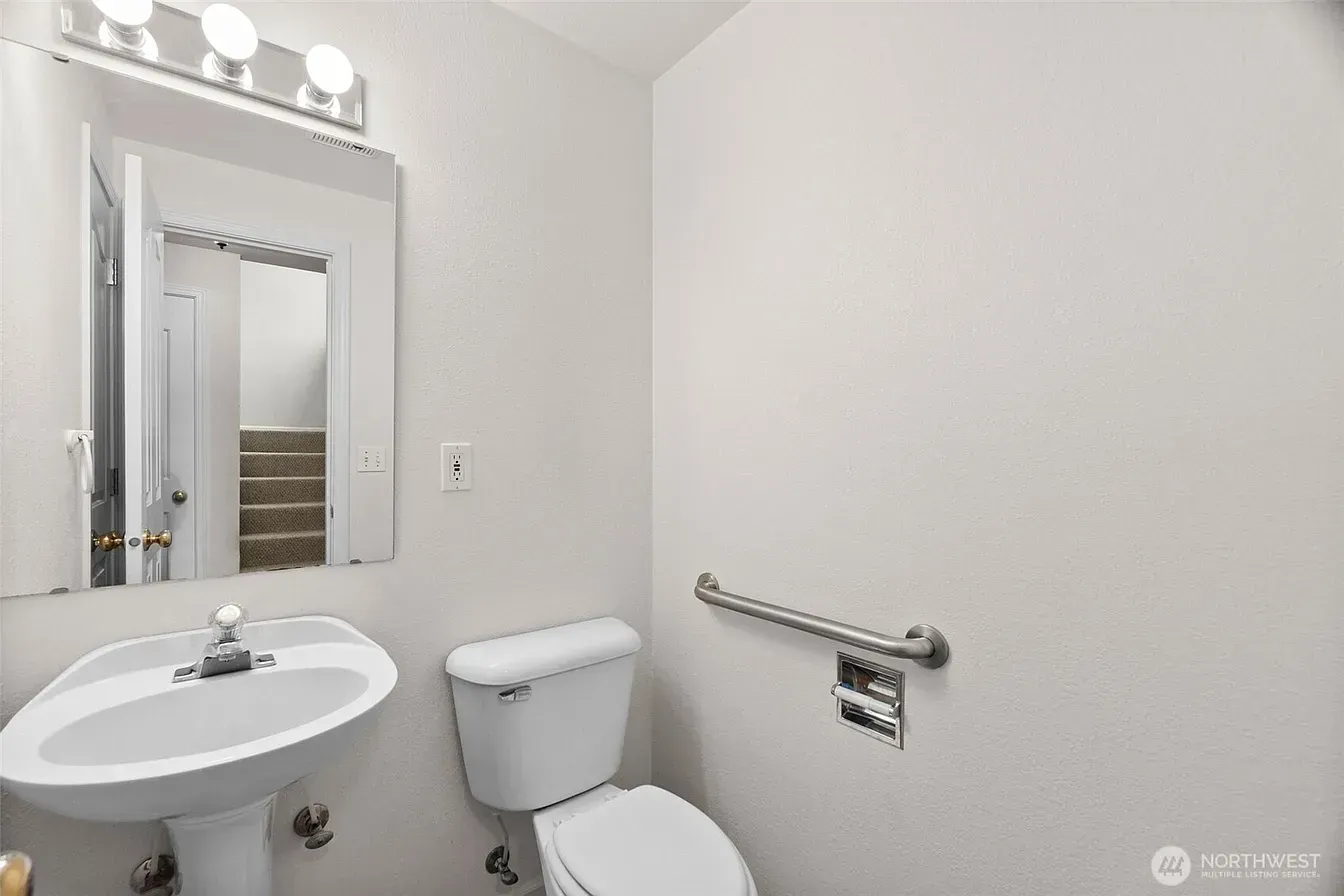 Small white bathroom with sink, mirror, toilet, and grab bar on the wall.