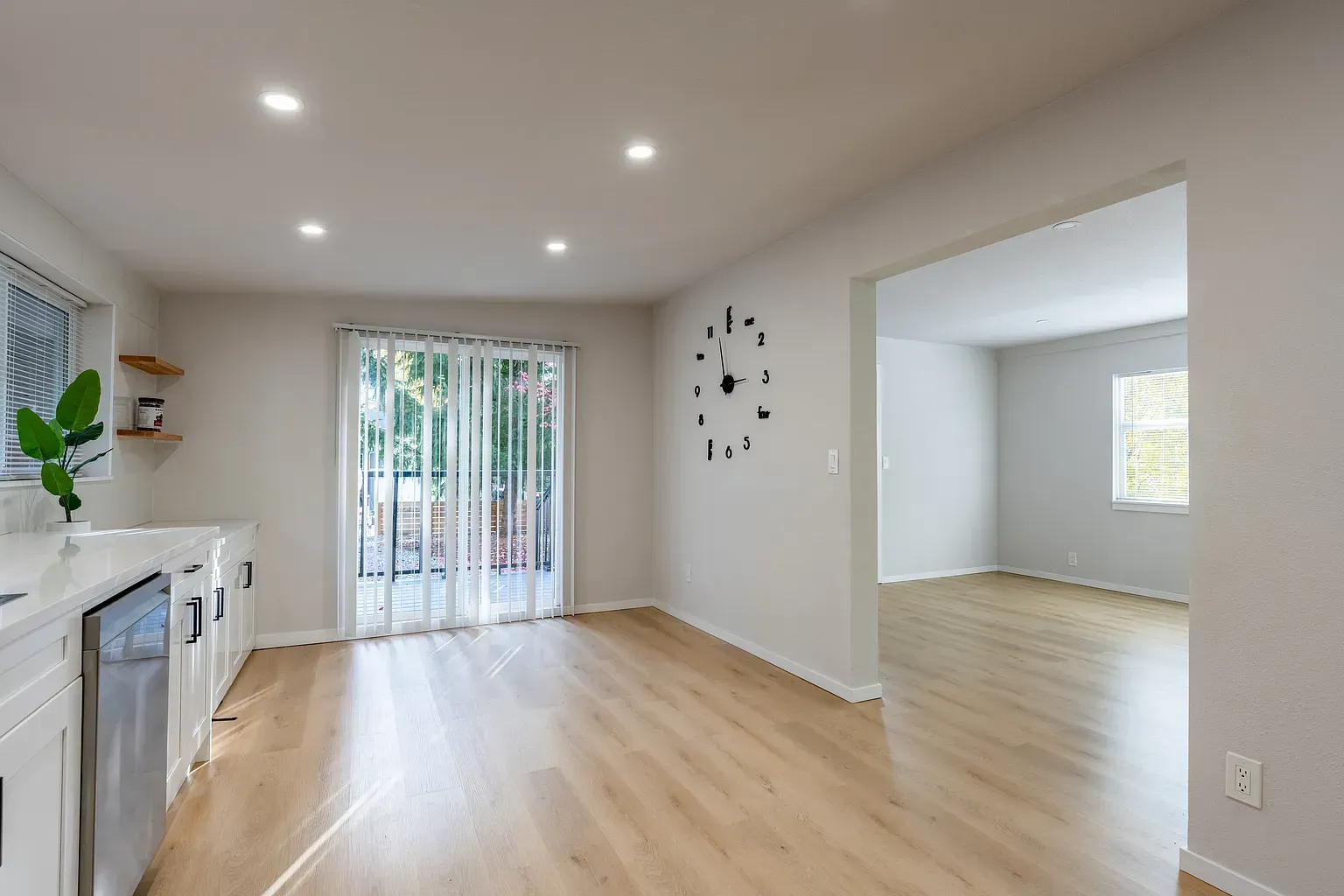 Bright open kitchen and dining area with light wood floors, white walls, and sliding glass doors.