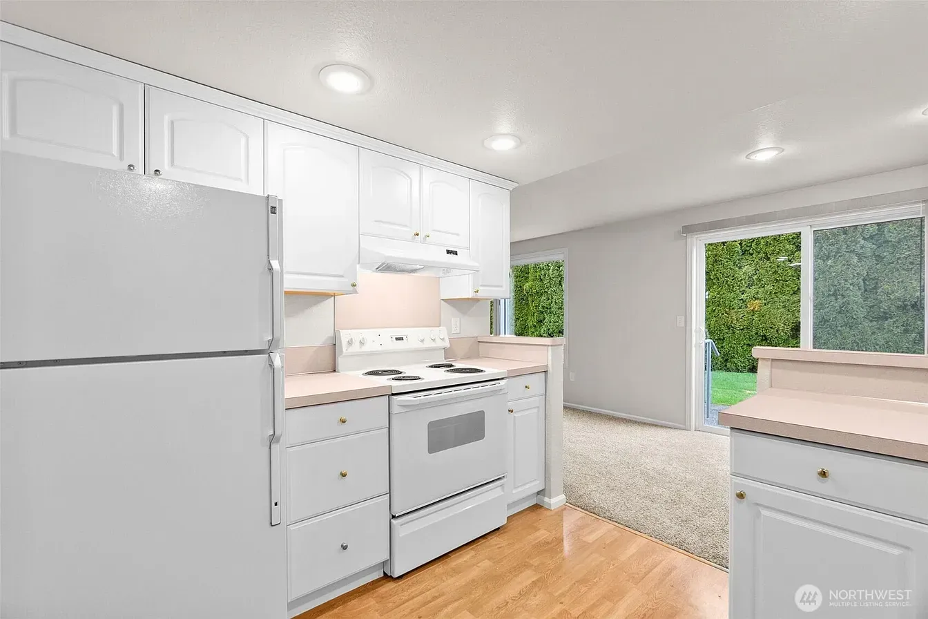 Bright white kitchen with stainless appliances, wood floor, and sliding glass door to a green backyard.