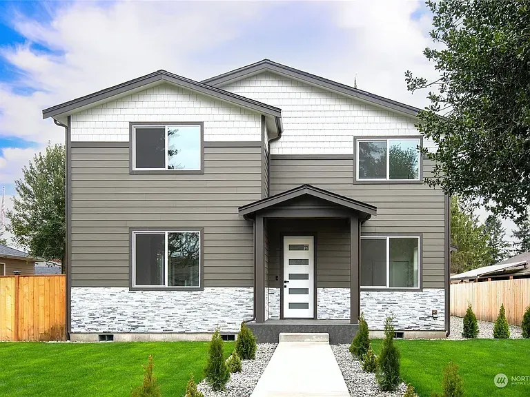 Two-story house with gray and white siding, stone base, and a pathway to the front door.