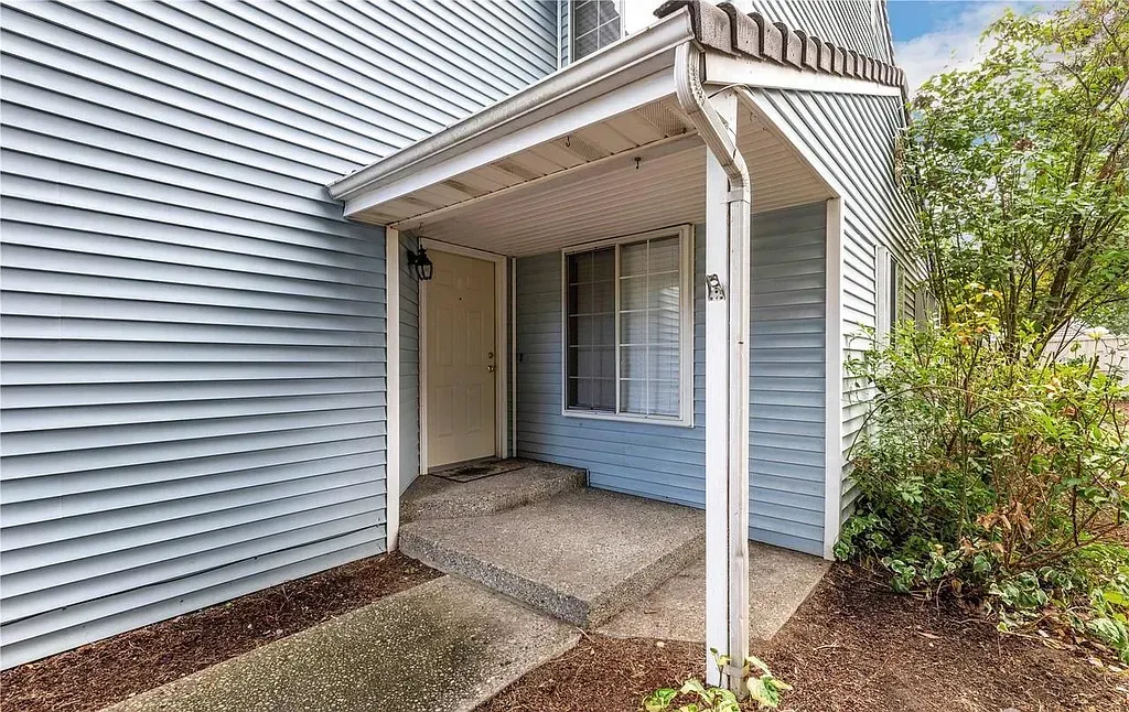 Entrance to a townhouse with a covered porch and small concrete steps. Blue siding and a window.