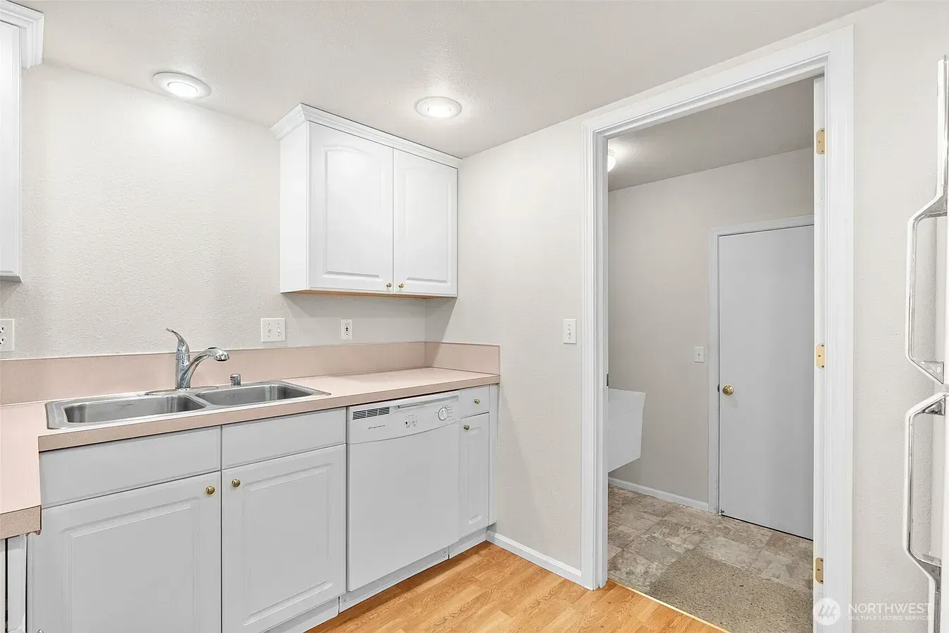 Bright white laundry room with sink, cabinets, and a doorway to a tiled utility area