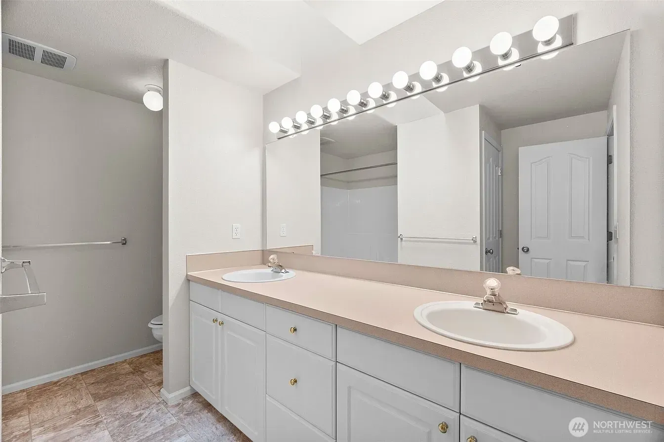 Bright bathroom with white cabinets, long mirror, double sink vanity, and beige countertop