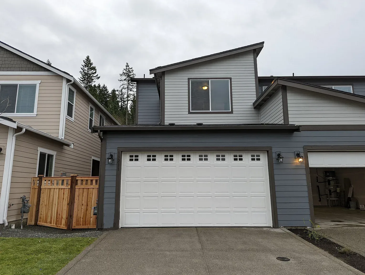 Gray and white townhome with a two-car garage, gray siding, and a sloped roof under a cloudy sky.