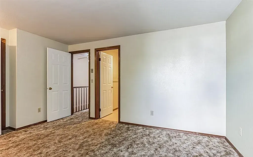 Bedroom with beige carpet, white walls, and three doors; one leading to a staircase.
