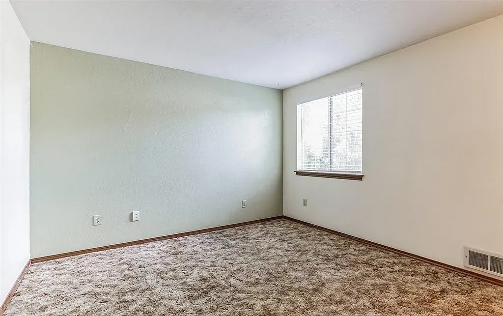 Empty room with green and white walls, brown carpet, window with curtain.