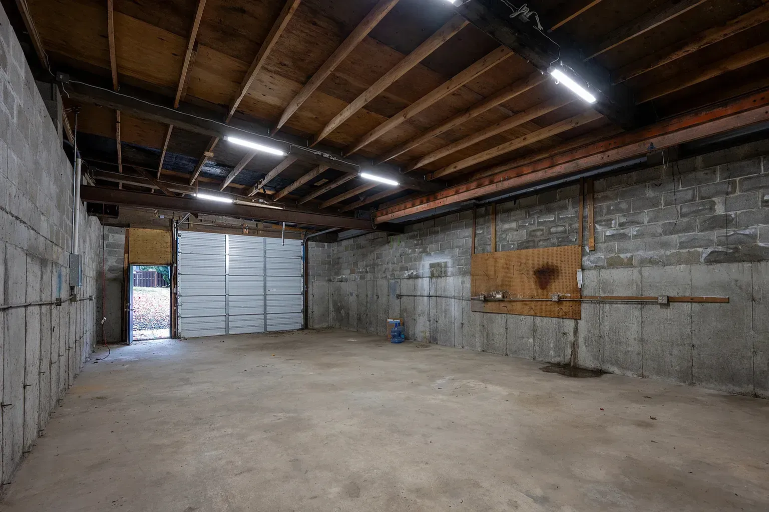 Empty warehouse interior with concrete floor, exposed beams, and large metal doors.