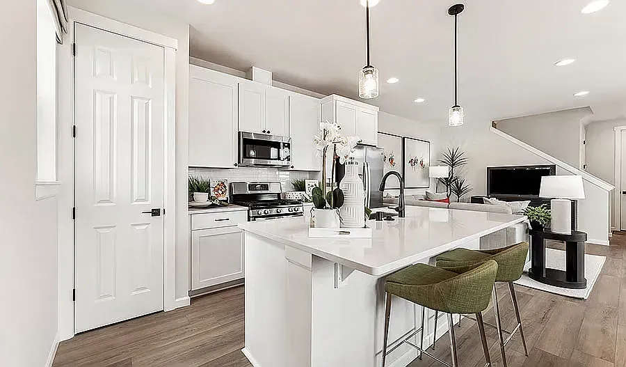 White modern kitchen with island, two green barstools, and hanging lights.
