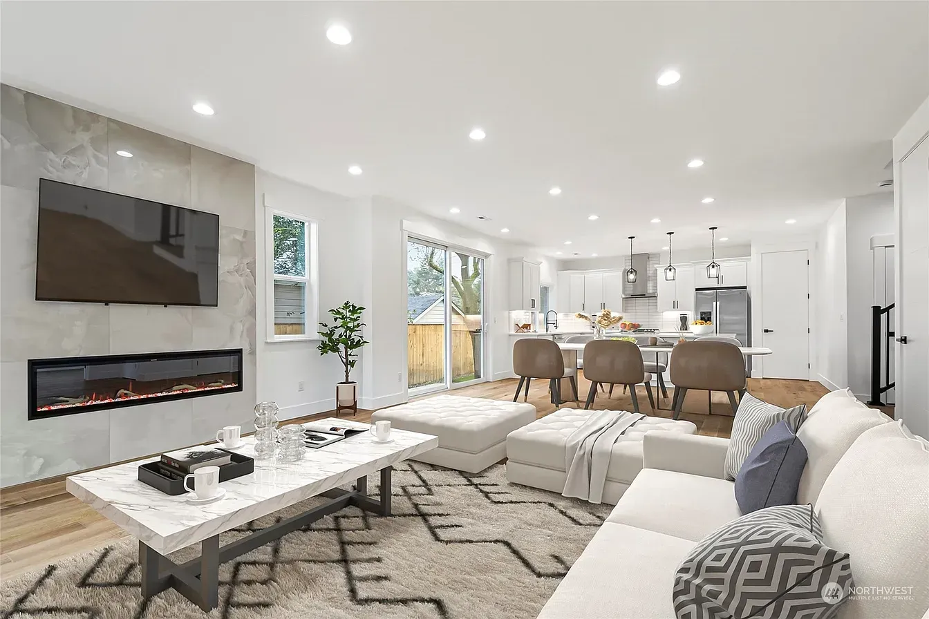 Modern living room with fireplace, kitchen, white walls, and wooden floors.