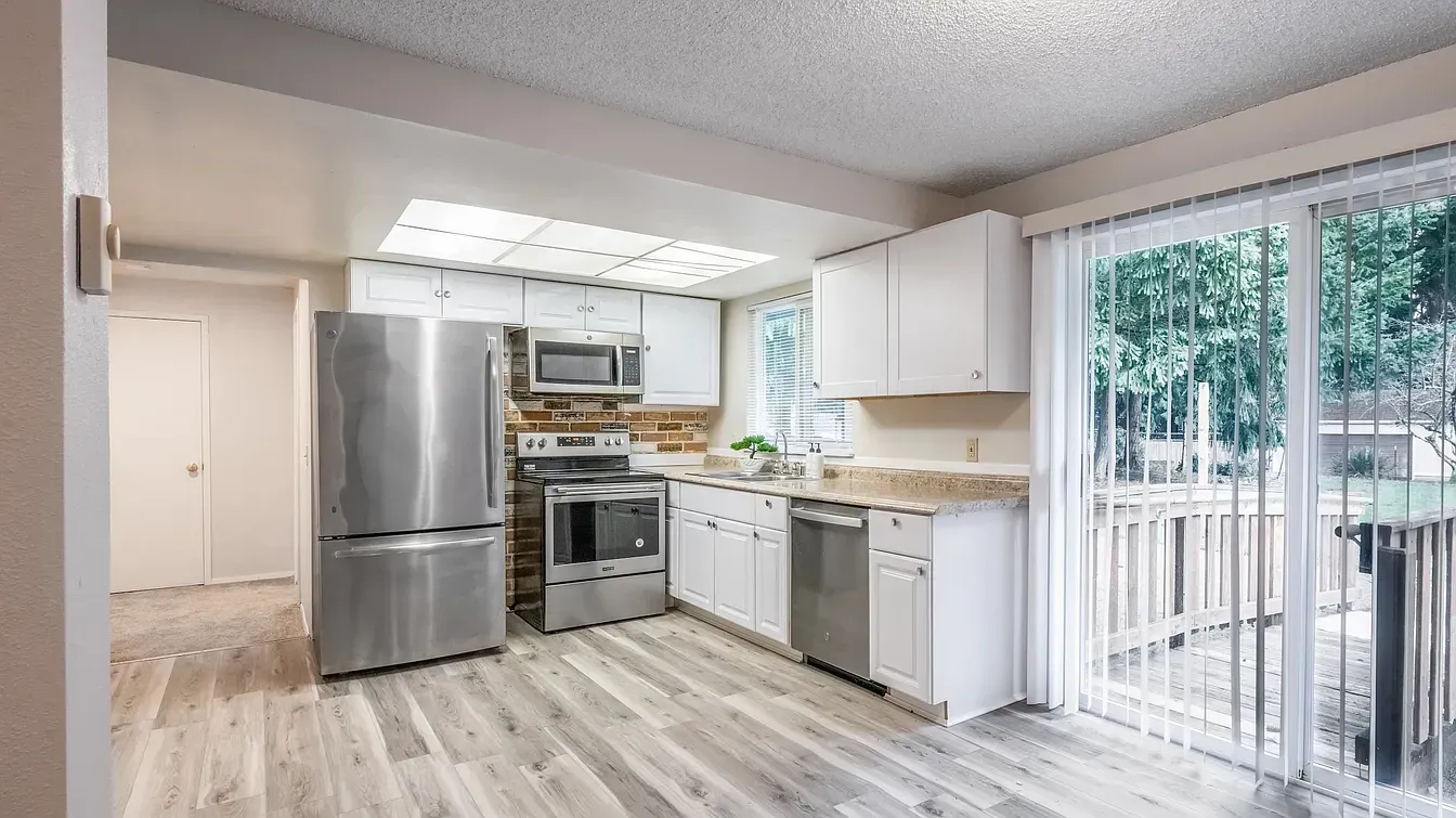 Kitchen with white cabinets, stainless steel appliances, and sliding glass door to a deck.