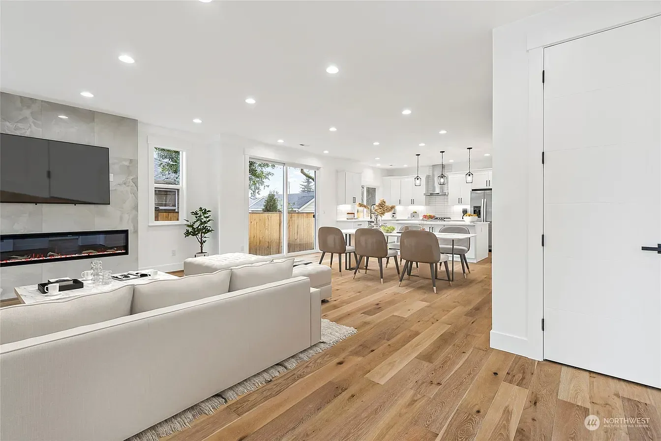 Bright, open-plan living space with a kitchen, dining area, and fireplace. Light wood floors and white walls.