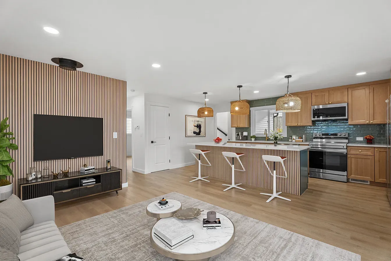 Modern open-plan kitchen and living room with wood accents, island stools, TV, and light hardwood floors