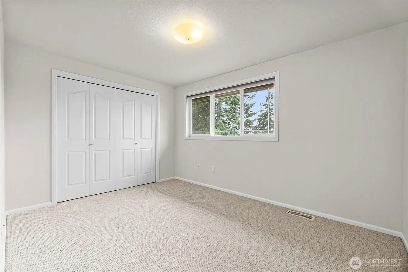 Empty white bedroom with carpet, closet doors, and a window