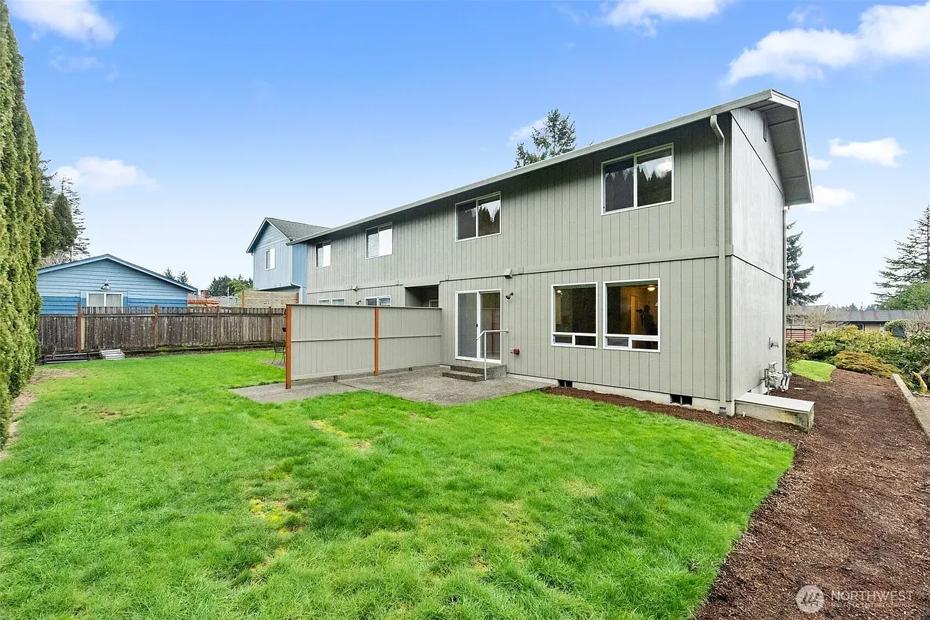Two-story gray house with a green backyard and wooden fence on a cloudy day