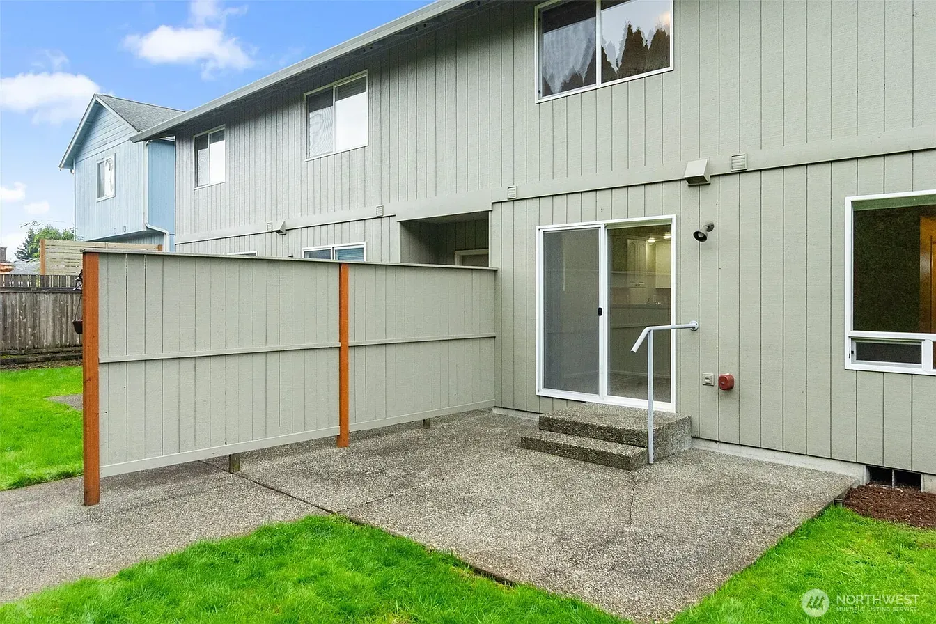 Backyard patio beside a gray two-story house with sliding glass door and gravel yard