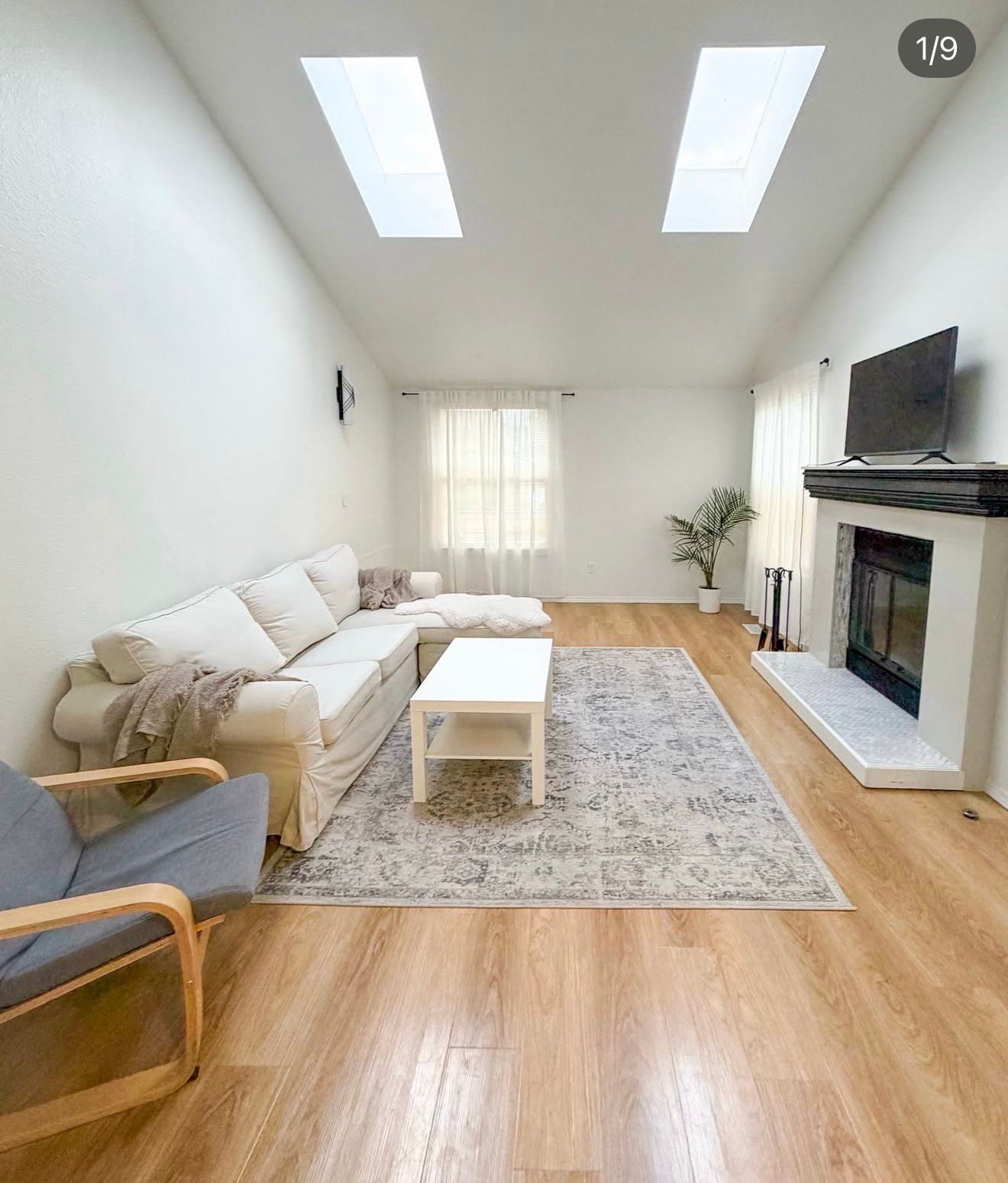 Living room with white walls, skylights, light wood floors, and neutral-toned furniture.