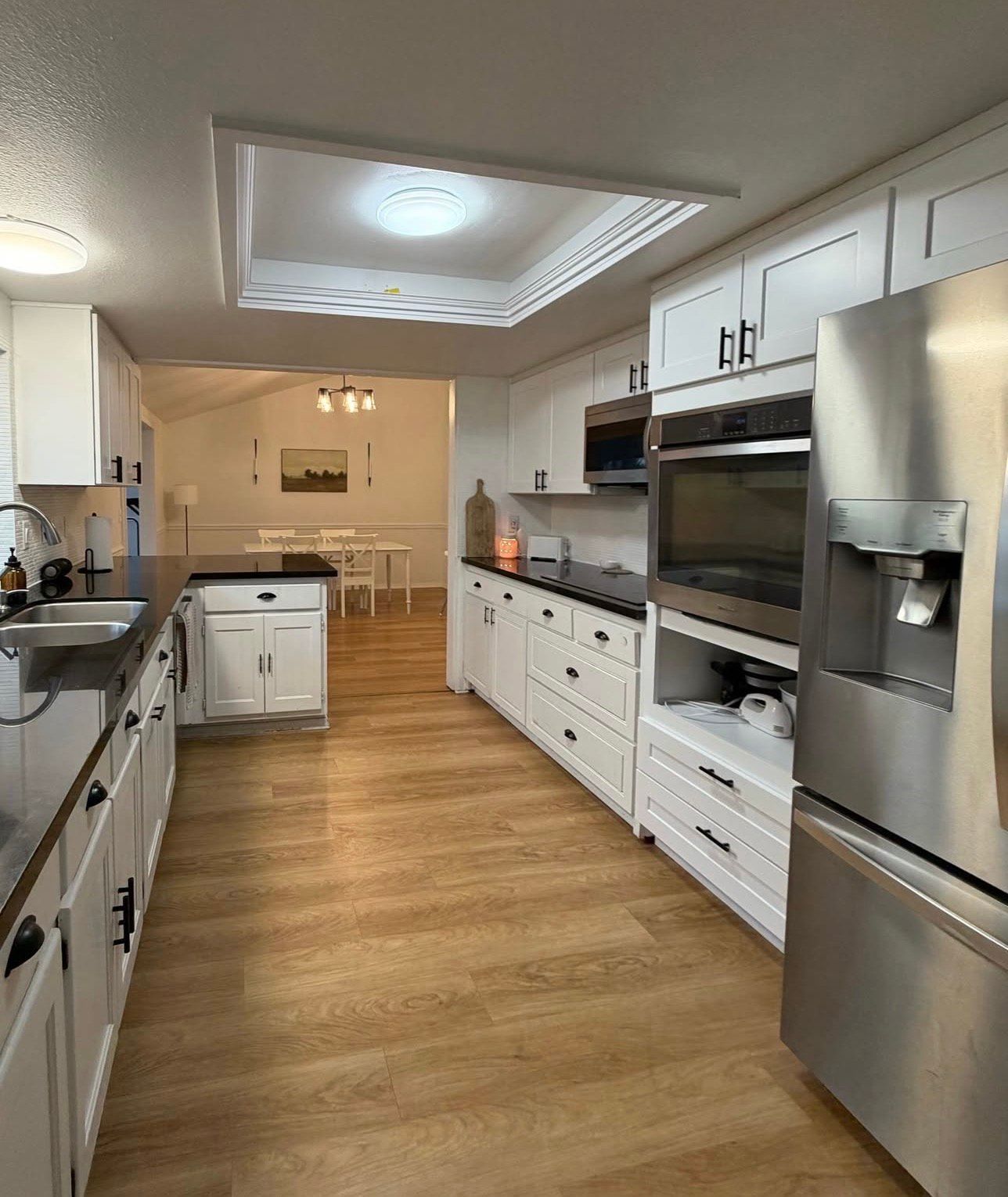 White kitchen with black countertops, stainless steel appliances, and wood-look flooring.