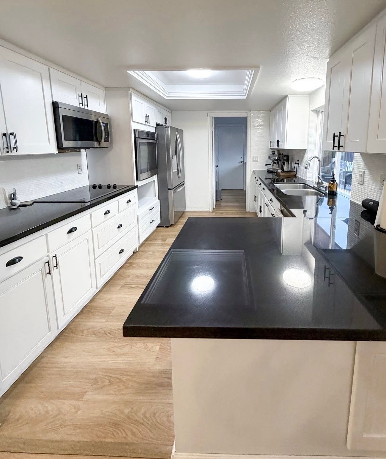 Bright kitchen with white cabinets, dark countertops, and stainless steel appliances.