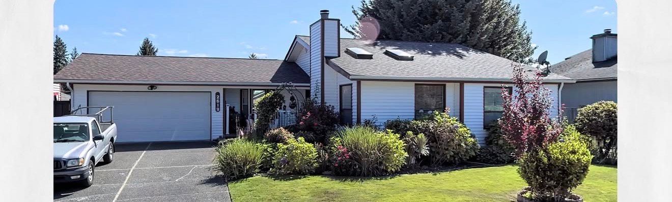 A white house with a garage and green lawn, with a truck parked in the driveway.
