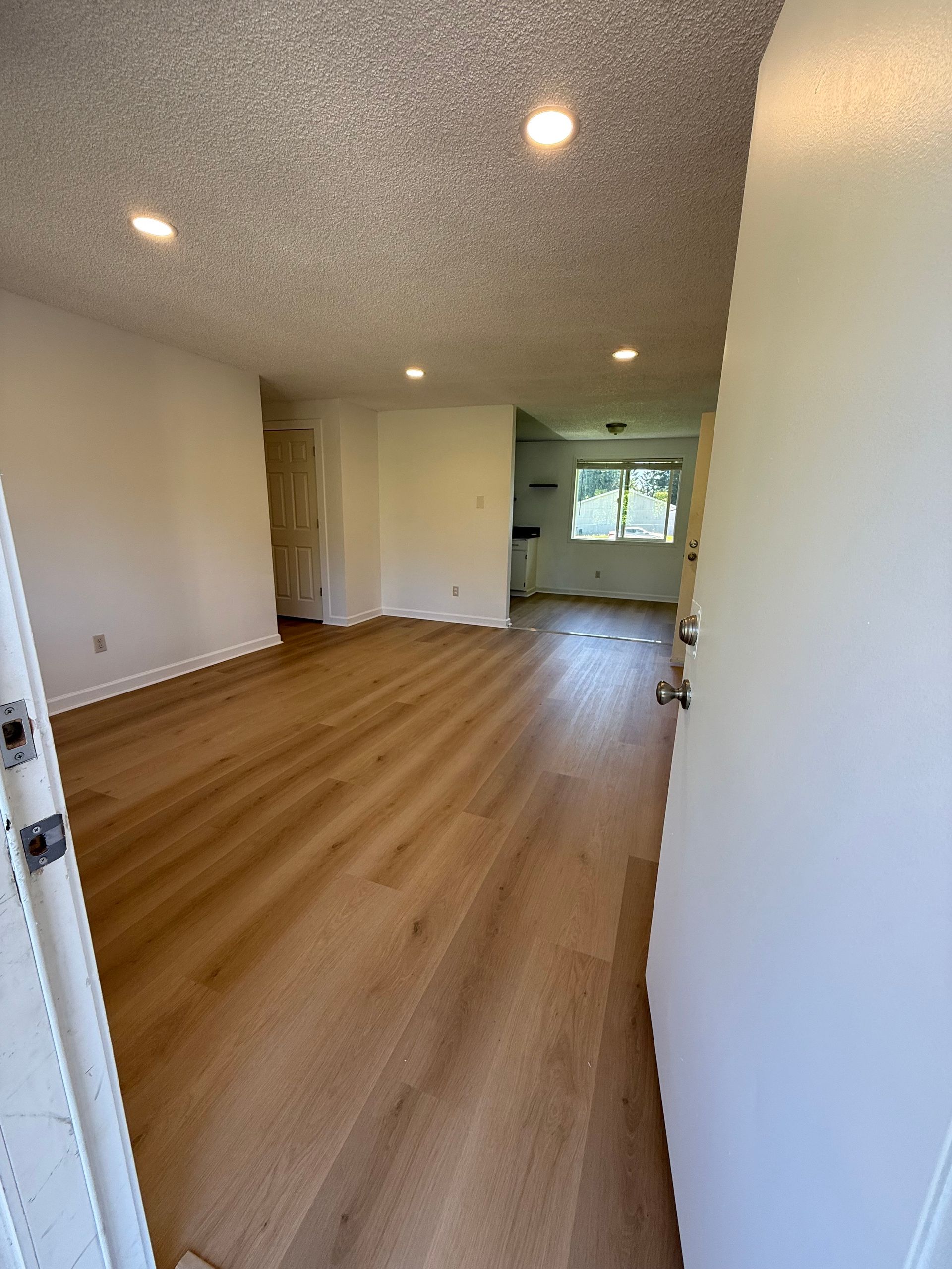 Interior view of a room with wood-like flooring, white walls, and a recessed ceiling. Open doorway on the right.