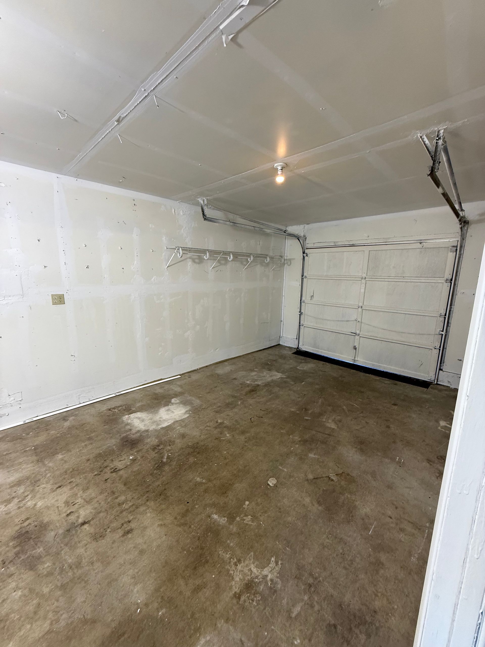 Empty garage interior with a concrete floor, drywall walls and ceiling, and a closed garage door.