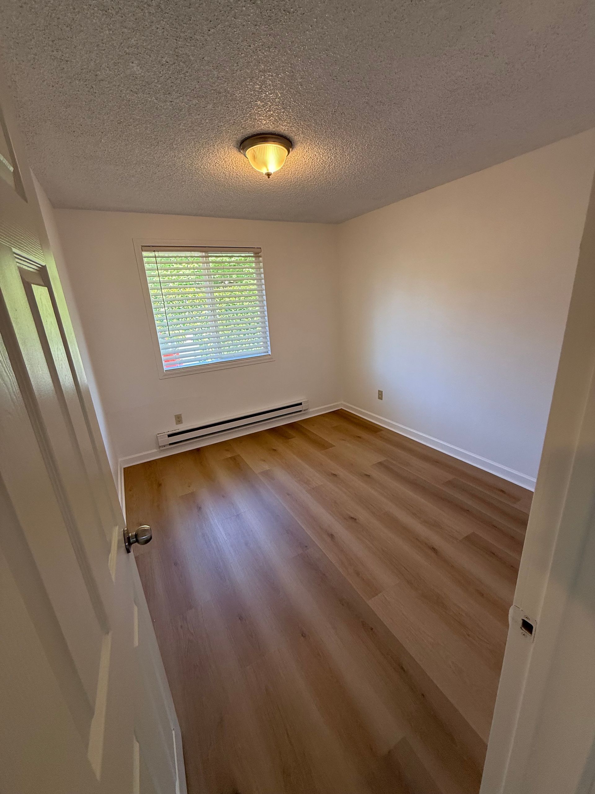 Empty room with wooden floors, small window, and ceiling light.