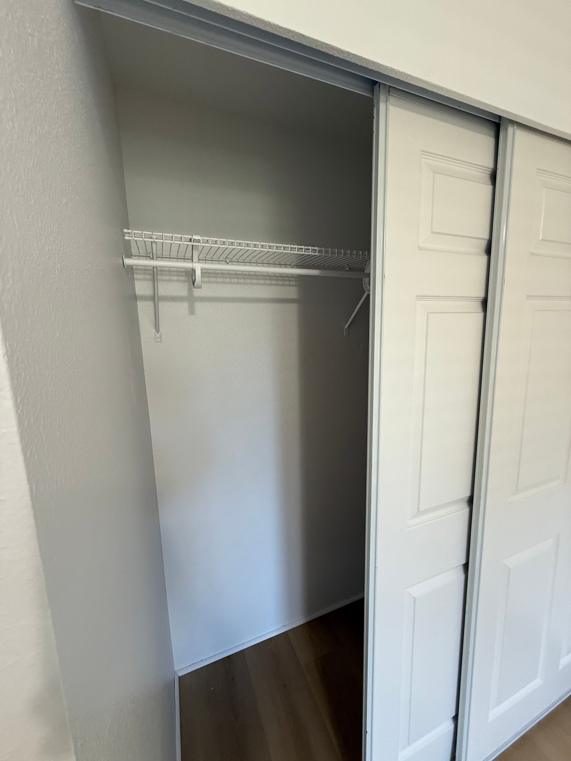 Empty closet with white sliding doors; a shelf and hanging rod are inside.
