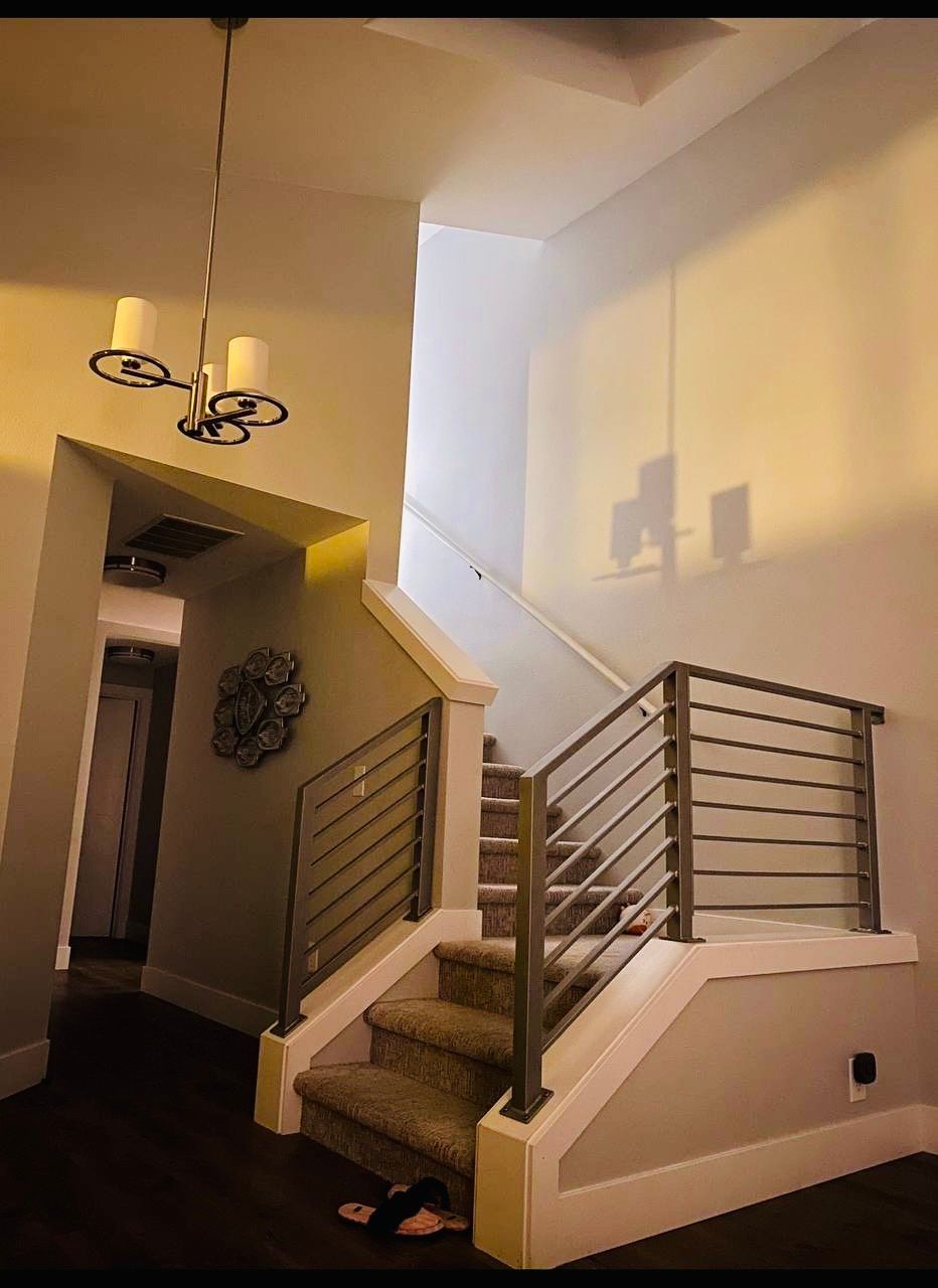 Staircase with modern metal railing, carpeted steps, and chandelier. Entrance to left, light walls.