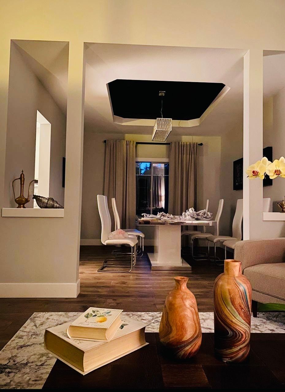 Modern dining room visible through an archway, featuring table set for dinner and a long chandelier.