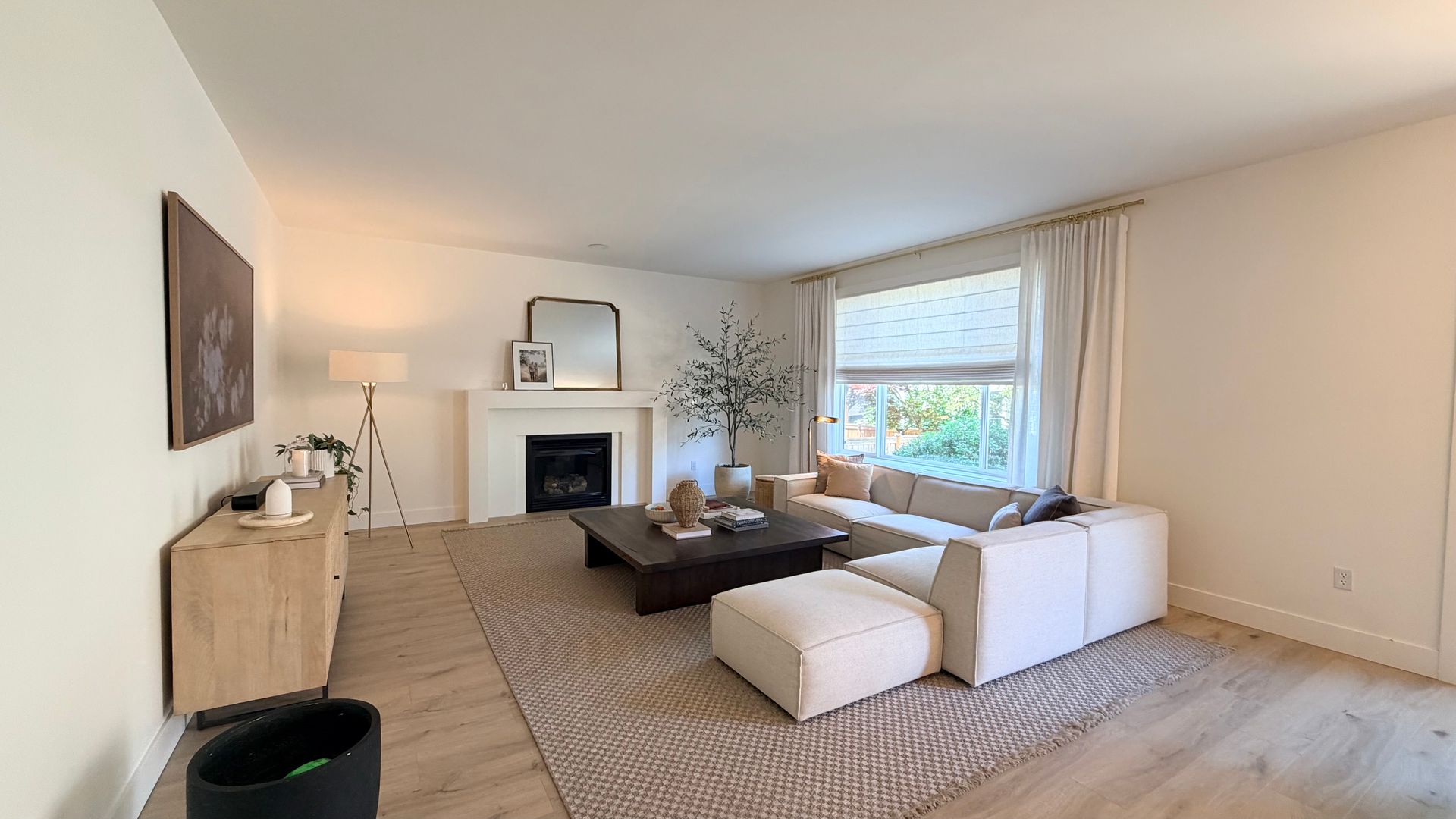 Bright living room with white sectional sofa, fireplace, large window, and neutral decor