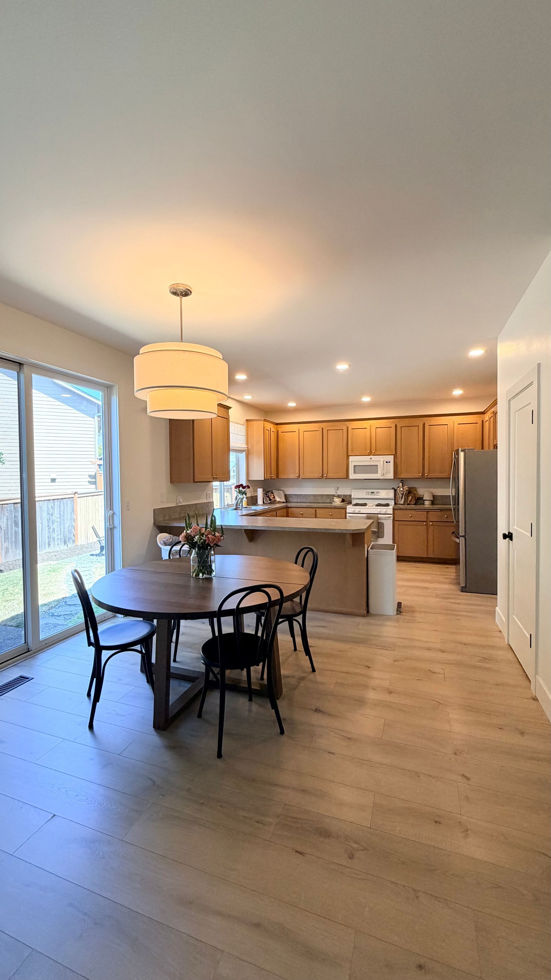 Bright open-plan kitchen and dining area with wood floors, white walls, and a table by large windows.