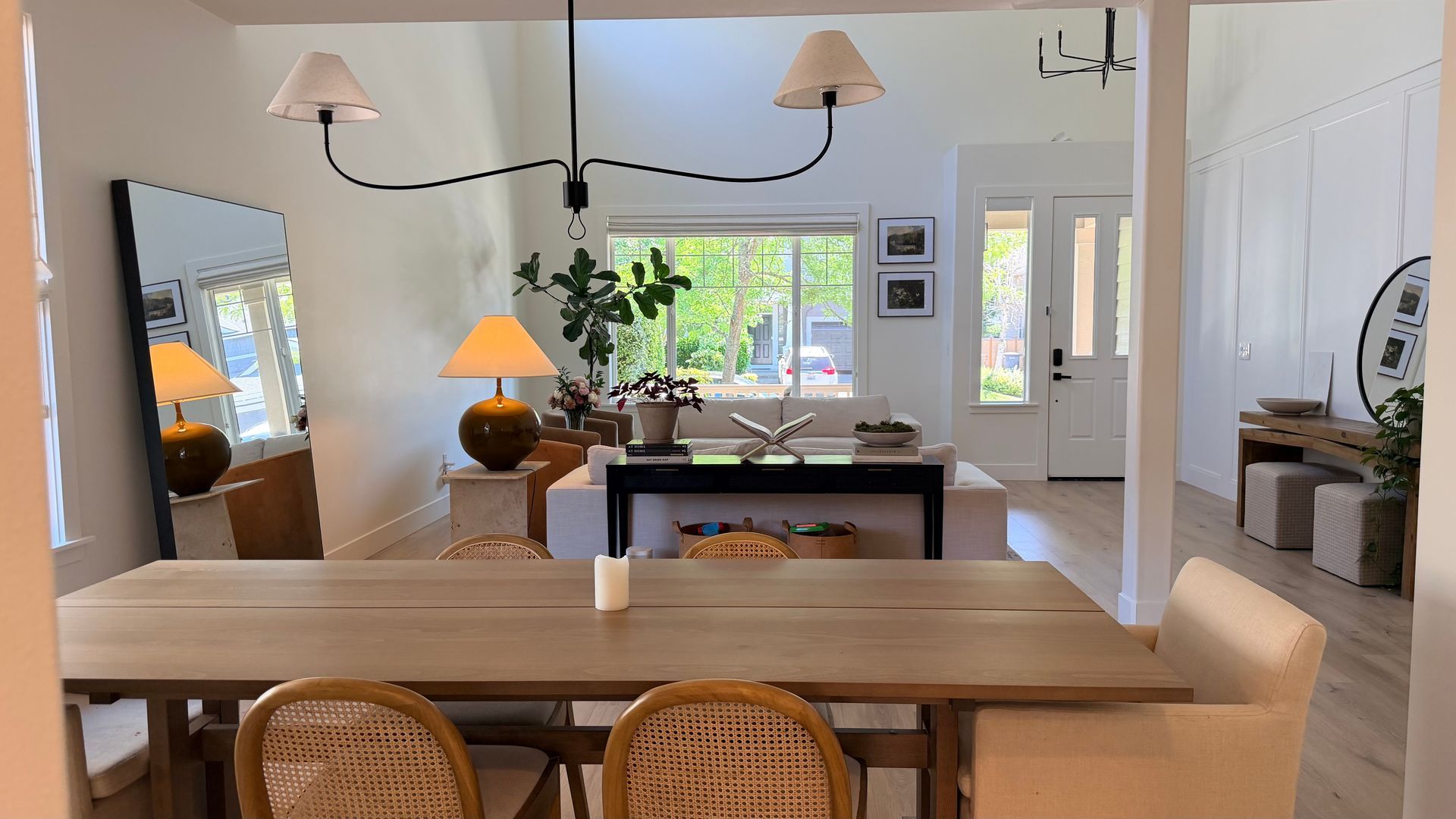 Bright, airy dining room with wooden table, woven chairs, lamps, and a large window.