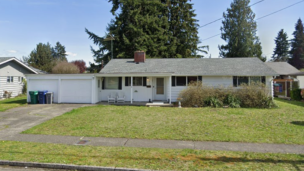 A one-story white house with attached garage, green lawn, and trees on a sunny day.