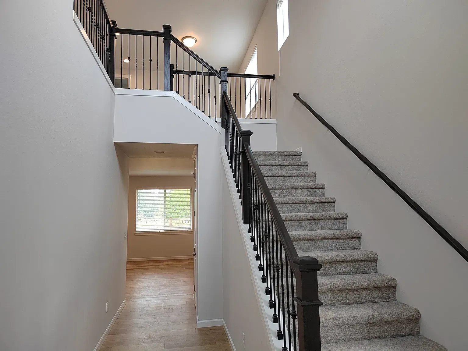 Interior view of a staircase with black railing and carpeted stairs, leading up to a landing.