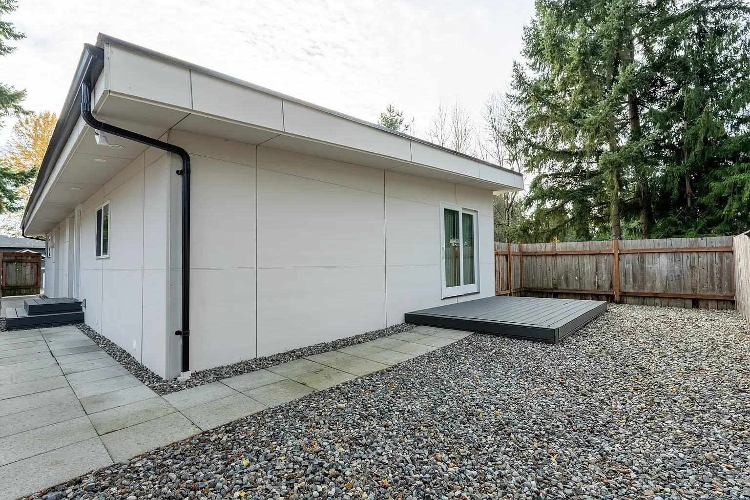 Modern white house exterior with gravel yard, concrete walkway, and fenced backyard.