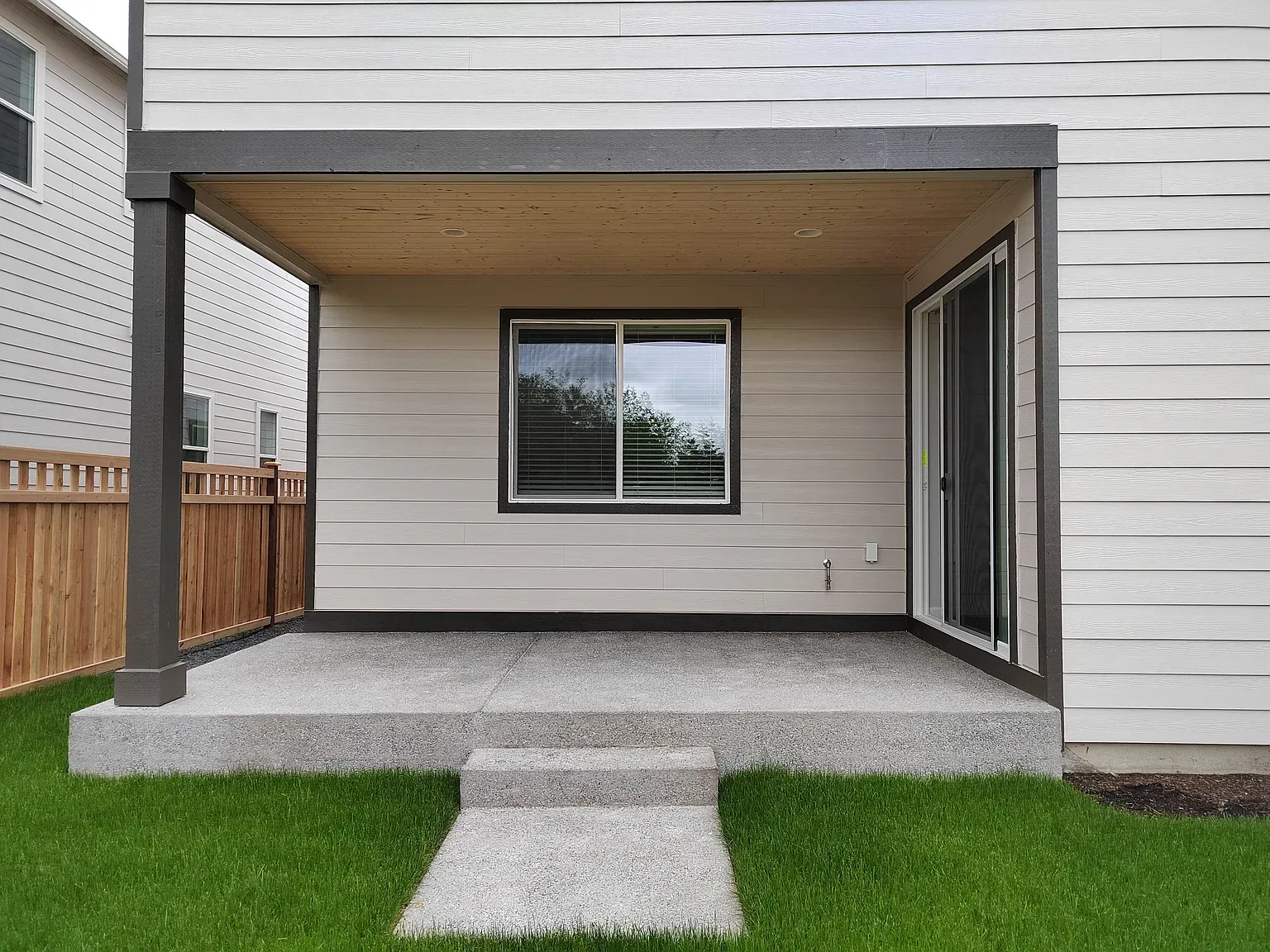 Covered patio with concrete floor, steps, and window, adjacent to a sliding glass door and fenced yard.