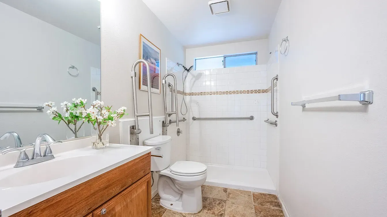 Bathroom with accessible features: grab bars, roll-in shower, raised toilet, and sink.