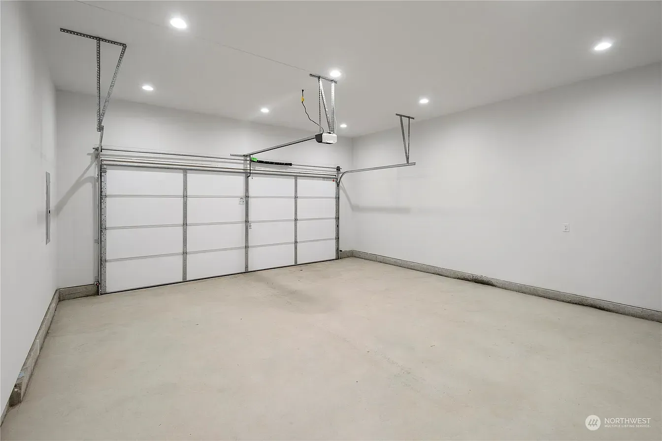 Empty garage with white walls, a closed white garage door, and a concrete floor.
