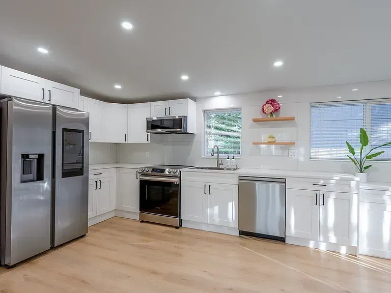 Bright modern kitchen with stainless steel appliances, white cabinets, and light wood flooring