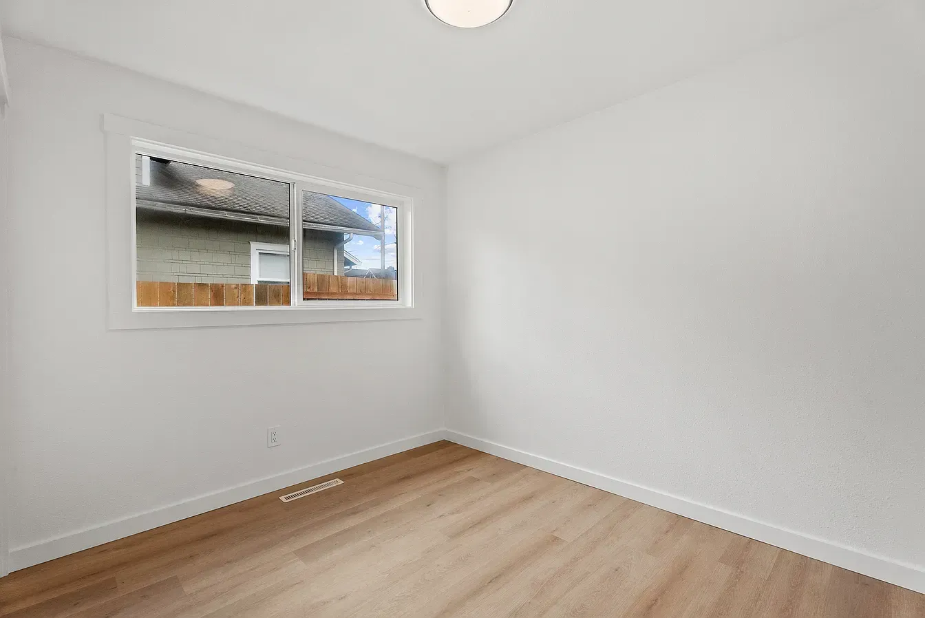 Empty white room with light wood floor and a window letting in daylight.