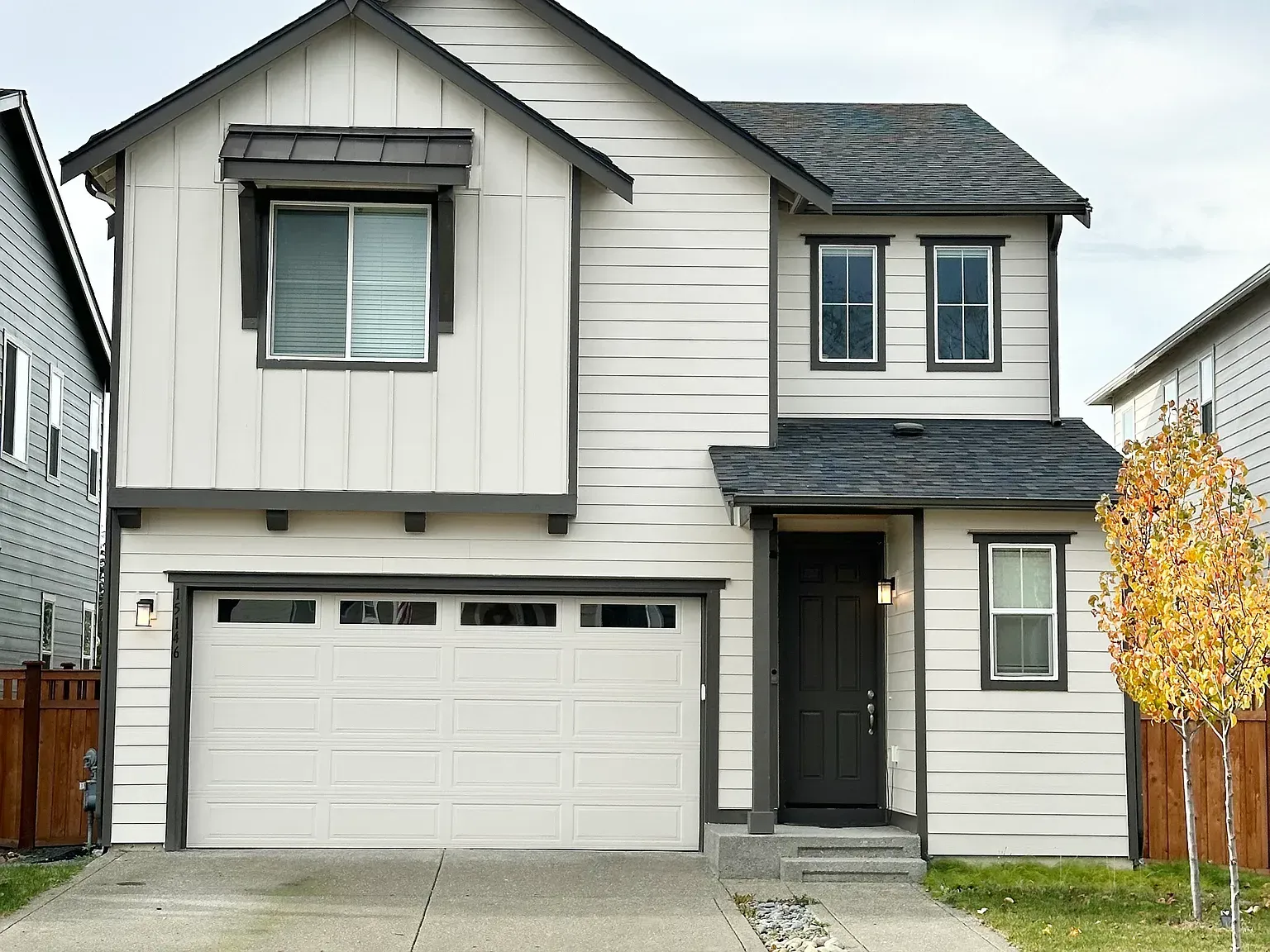 Two-story house with gray siding, white trim, and a gray roof. Garage door closed.