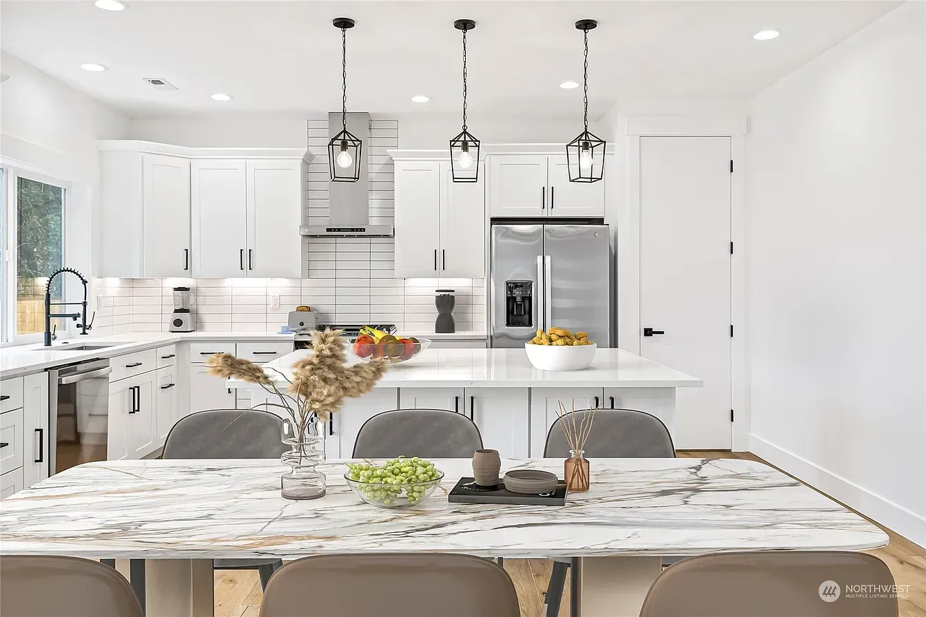 Modern white kitchen with island, pendant lights, stainless steel appliances, and dining table.