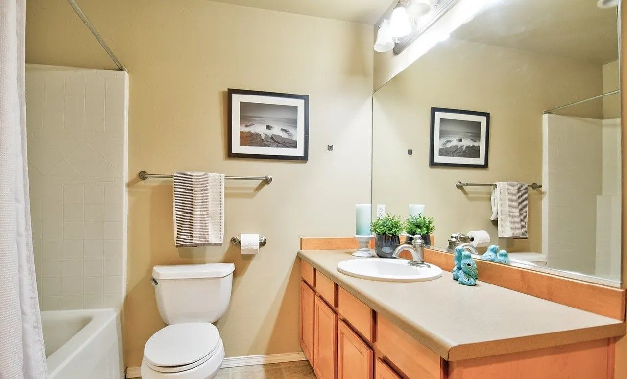 Bathroom with beige walls, a white tub and toilet, and a long counter with a mirror.