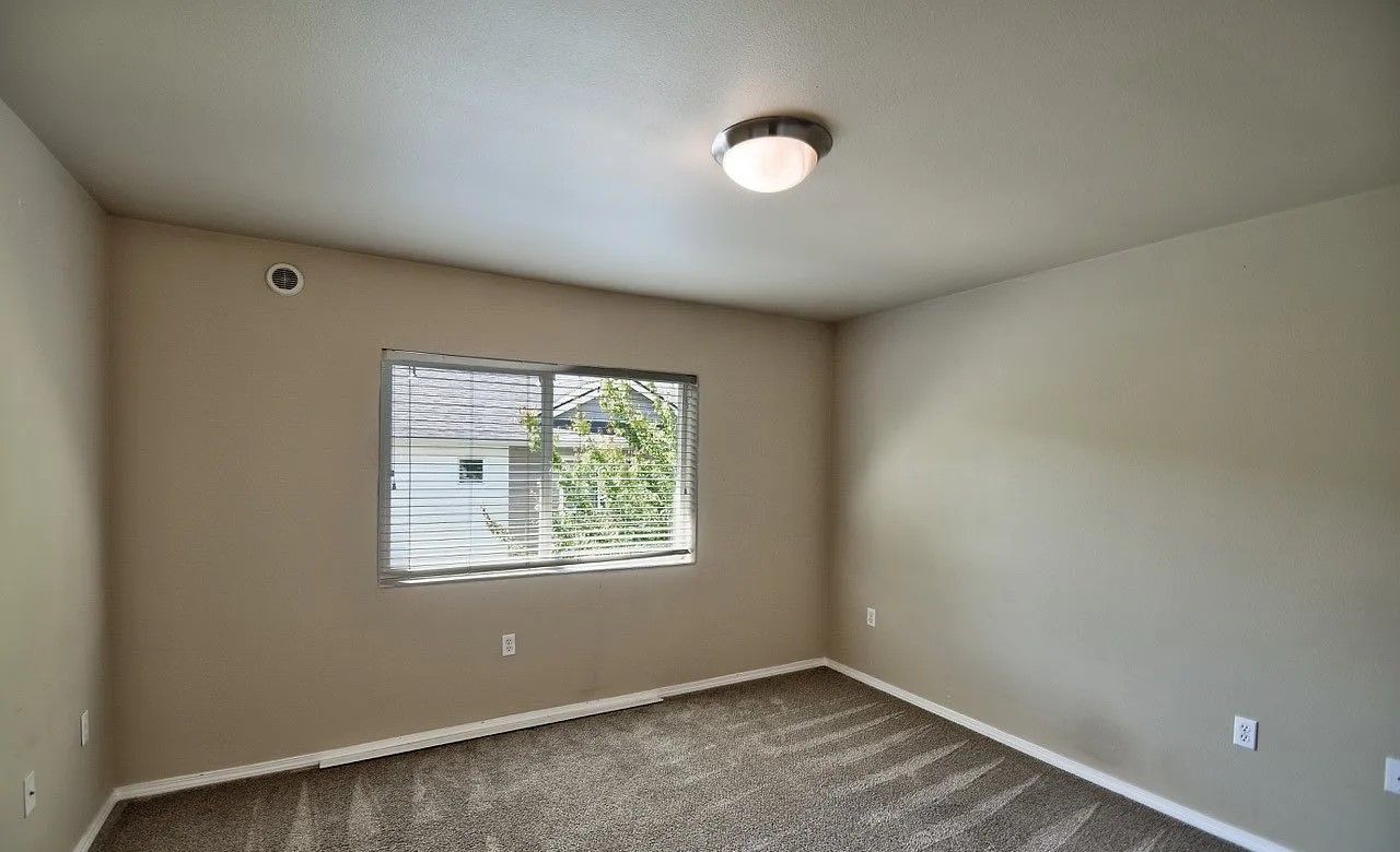 Empty room with beige walls, a window, carpeted floor, and a ceiling light.